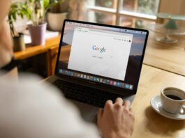 A person using a laptop displaying the Google homepage while sitting at a table with a cup of coffee.