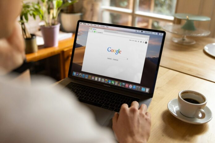 Google Opens Ad Platform to Prediction Markets in the U.S. A person using a laptop displaying the Google homepage while sitting at a table with a cup of coffee.