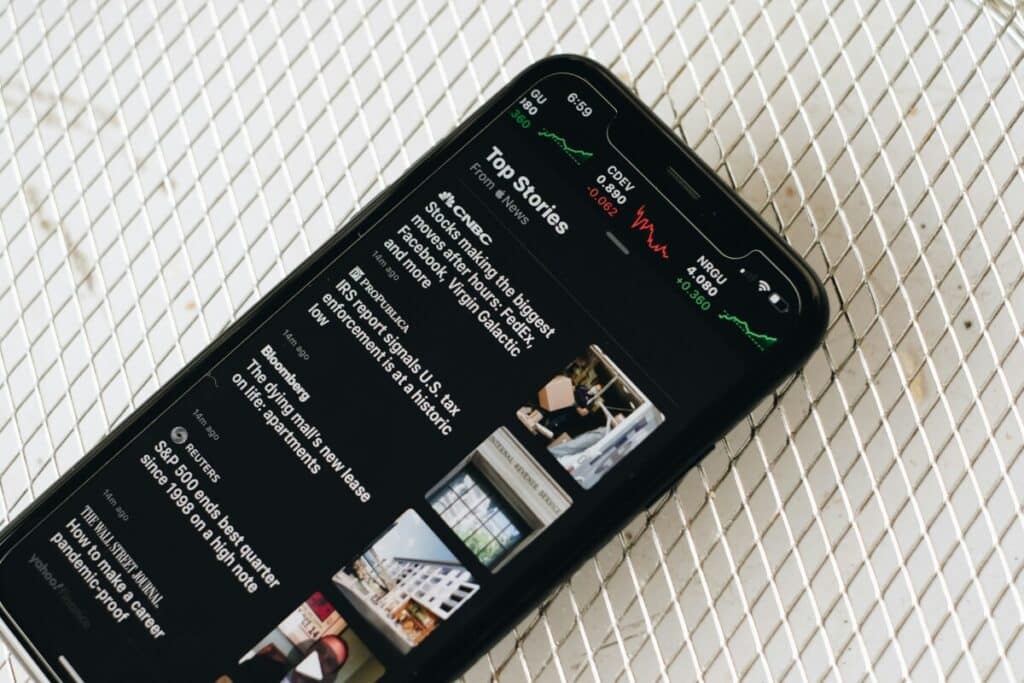 A smartphone displaying a news app with top headlines and stock market charts on the screen.
