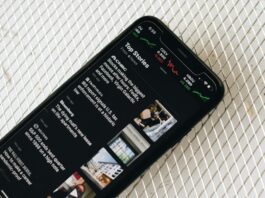 A smartphone displaying a news app with top headlines and stock market charts on the screen.