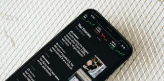 Polymarket Inks Exclusive Prediction Market Deal With The Wall Street Journal A smartphone displaying a news app with top headlines and stock market charts on the screen.