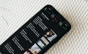 Polymarket Inks Exclusive Prediction Market Deal With The Wall Street Journal A smartphone displaying a news app with top headlines and stock market charts on the screen.