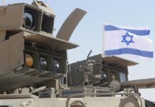 Israeli military equipment displayed beneath an Israeli flag during a defense exercise.