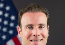 Portrait of CFTC Chariman Michael Selig in a suit standing in front of an American flag.