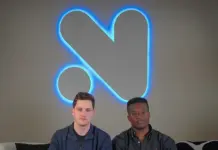 Novig founders seated on a couch beneath the company’s illuminated logo at the firm’s headquarters.