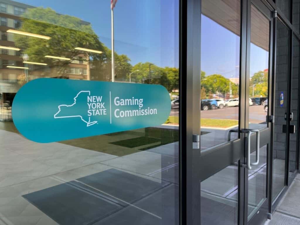 Entrance to the New York State Gaming Commission building with the agency’s logo displayed on the glass door.