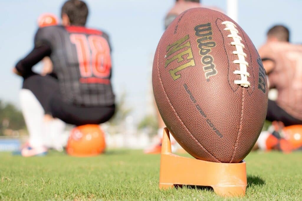 An NFL football on the field during a team practice, with players blurred in the background