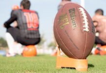 NFL Survey Shows Bettors Regularly Target Players Over Lost Bets An NFL football on the field during a team practice, with players blurred in the background