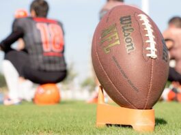 NFL Survey Shows Bettors Regularly Target Players Over Lost Bets An NFL football on the field during a team practice, with players blurred in the background