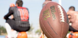 NFL Survey Shows Bettors Regularly Target Players Over Lost Bets An NFL football on the field during a team practice, with players blurred in the background