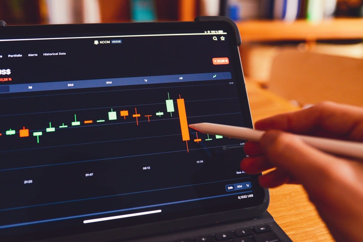 Person using a stylus on a tablet showing a financial trading chart