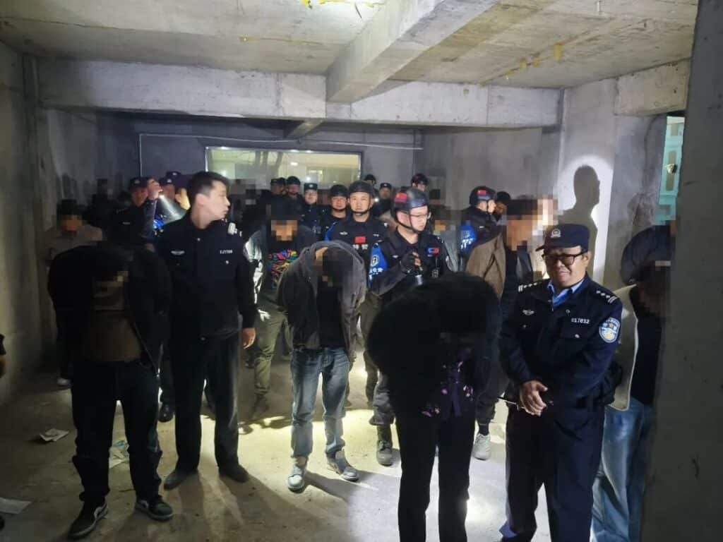 Chinese police officers with suspects arrested during a raid on an alleged gambling den in an abandoned building.