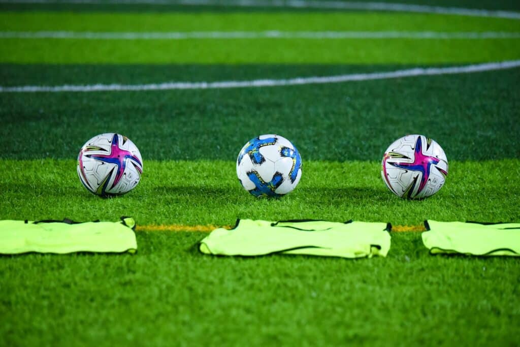 Three soccer balls and bibs on a field.