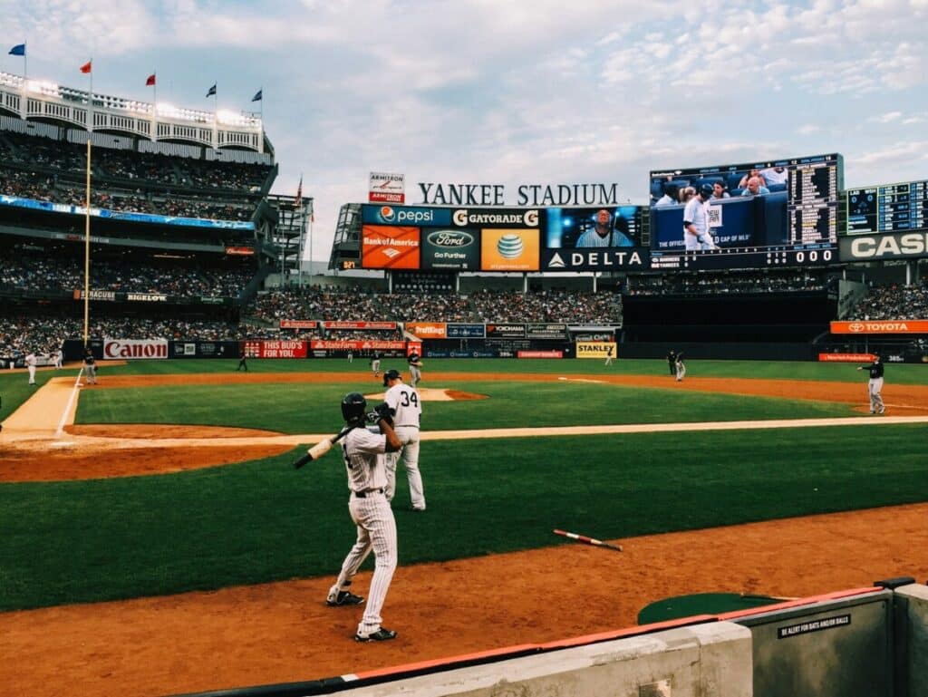 Yankee Stadium during a baseball game, with players on the field, fans in the stands, and advertising visible around the ballpark.